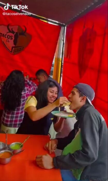 chica con uniforme de Coppel dando un taco a su novio con uniforme de Elektra 