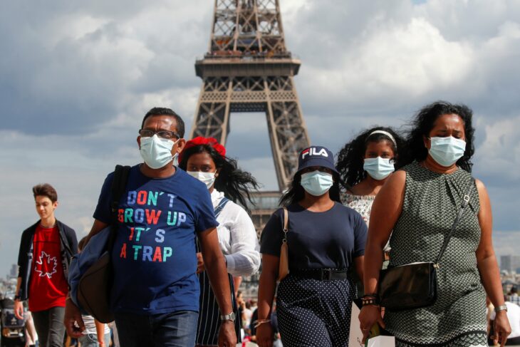 personas caminando con cubrebocas frente a la torre Eiffel en París 