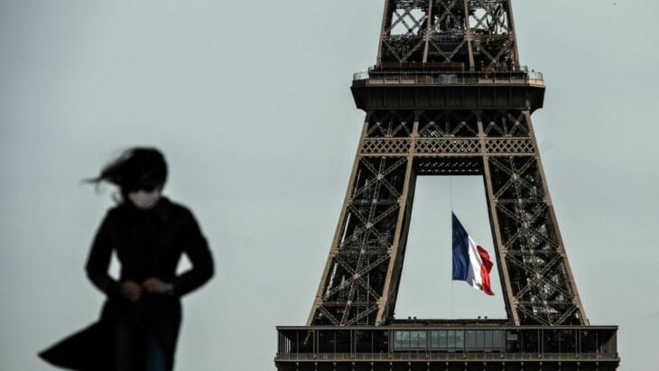 mujer con cubreboca caminando frente a la torre Eiffel en París, Francia