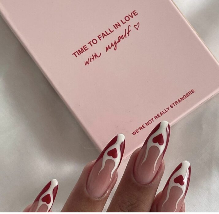 uñas sobre un libro rosa con diseño de llamas en color blanco combinadas con unos corazones en color rojo 