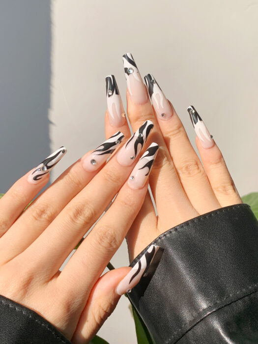 uñas acrílicas con diseño de llamas en color blanco y negro con algunas piedritas 