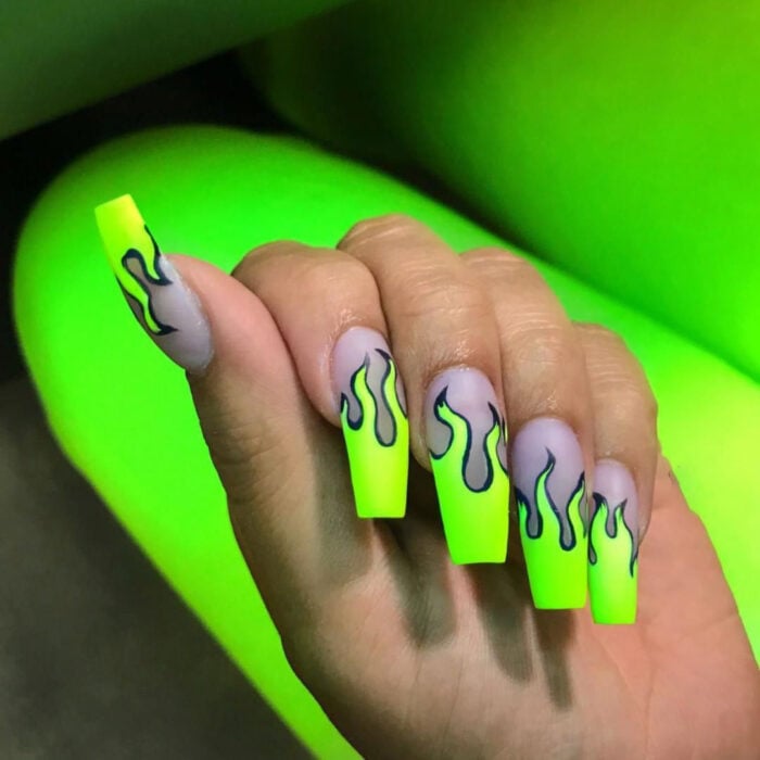 mano de una chica mostrando unas uñas acrílicas en forma de llamas color verde fluorescente 