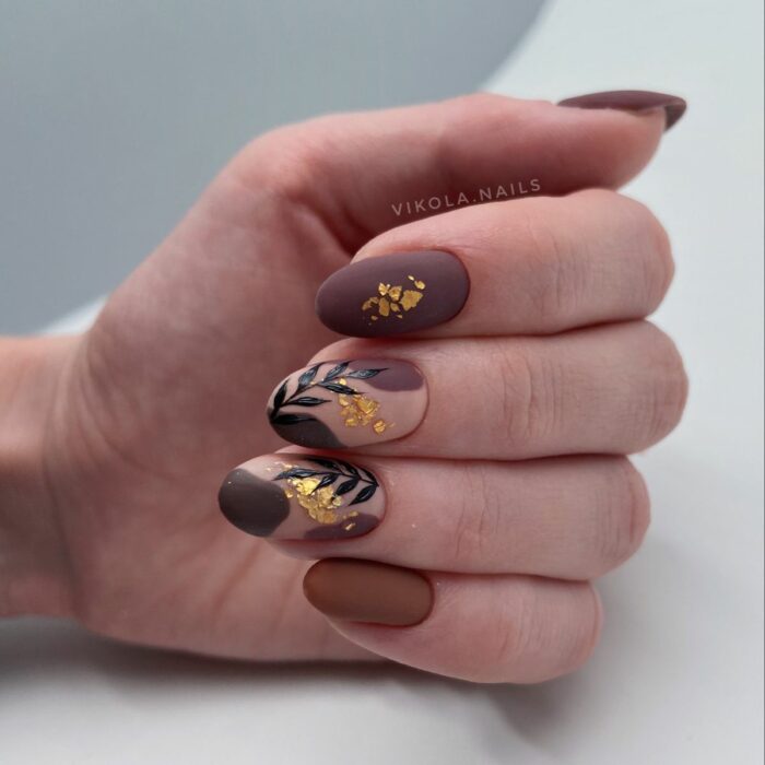 hand showing acrylic nails in strong tones with flower decoration with a bit of gold leaf 