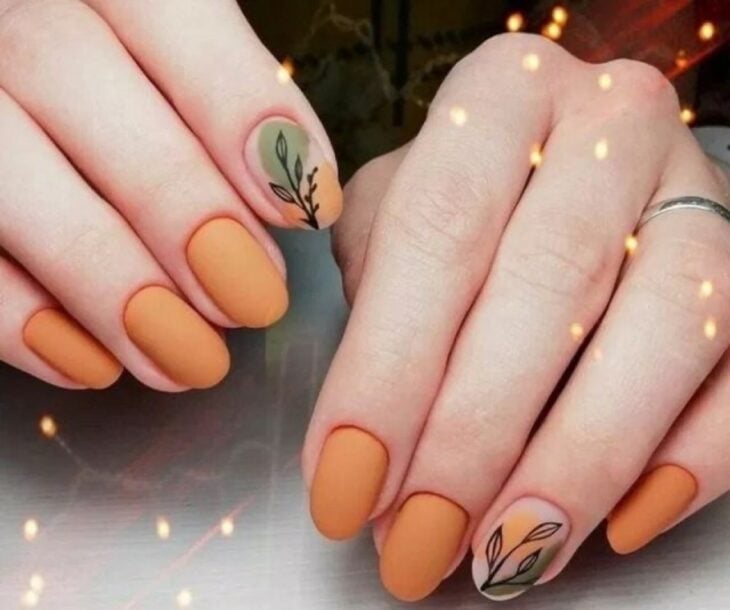 manos de una chica con uñas en color naranja con una del dibujo de una hoja 