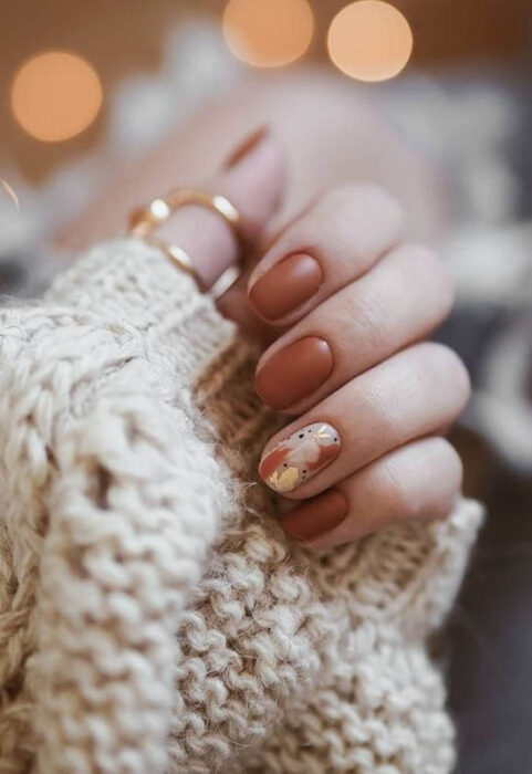 girl's hand showing nail design with dark color and autumn leaf design 