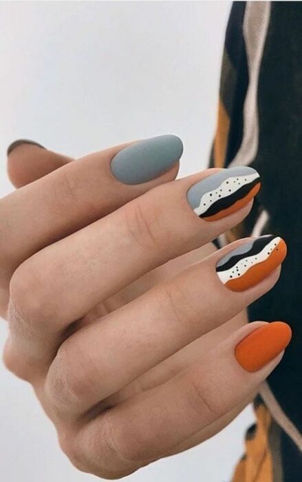 mano con diseño de uñas colorido en naranja con color azul grisáceo 