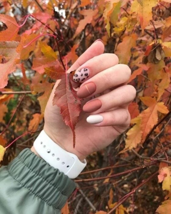mano mostrando diseño de uñas sobre unas hojas en otoño 