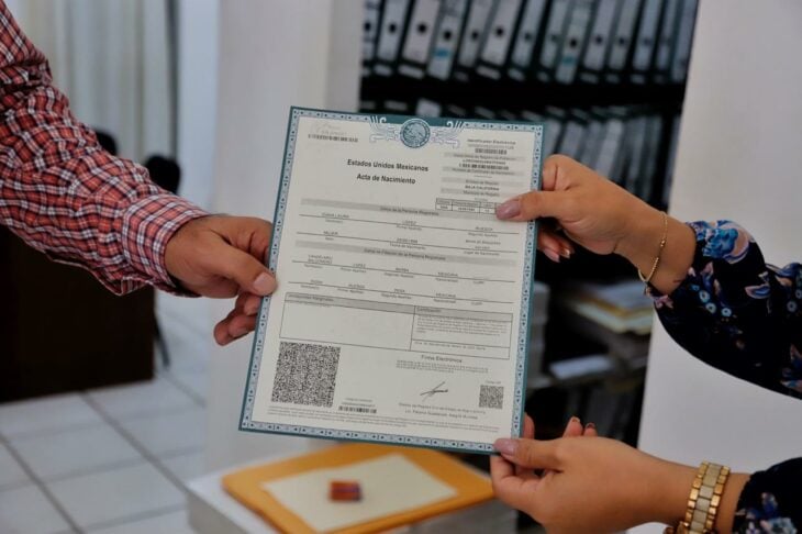 manos de una persona entregando una acta de nacimiento a otra en el registro civil 