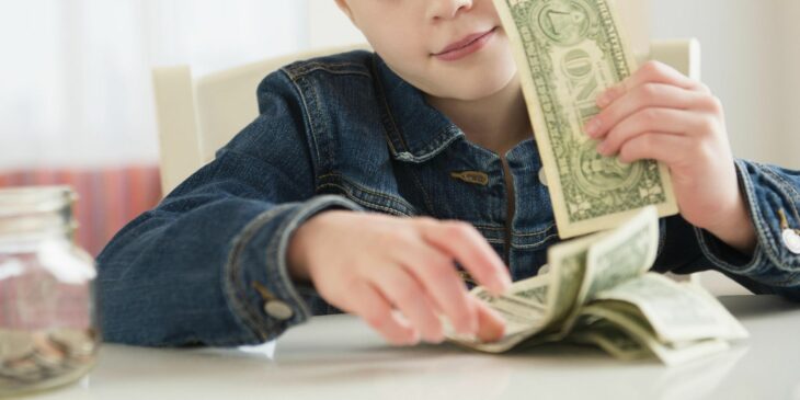 Niño con unos billetes mientras está sentado frente a una mesa 