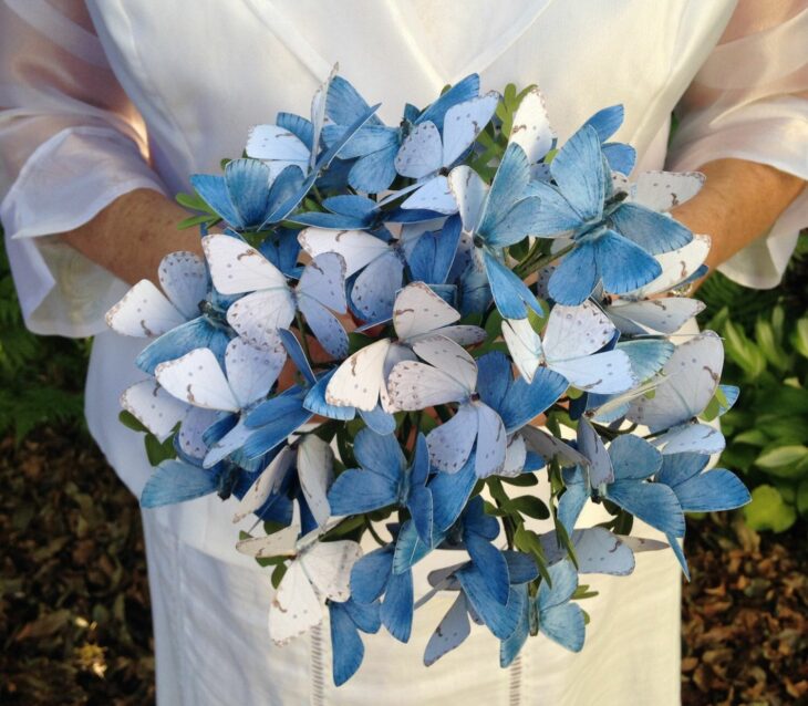 manos de una mujer con vestido de novia con un ramo hecho con mariposas en las manos 