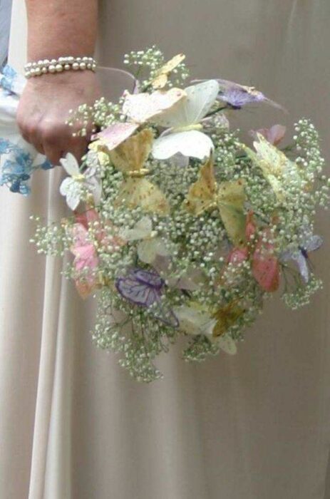 hand holding a bridal bouquet with paniculata and a couple of butterflies 