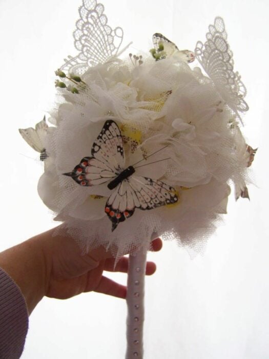 imagen de una mano mostrando un ramo de novia blanco con algunos detalles de mariposa 
