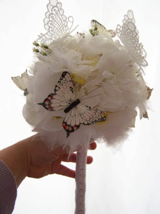 image of a hand showing a white bridal bouquet with some butterfly details 