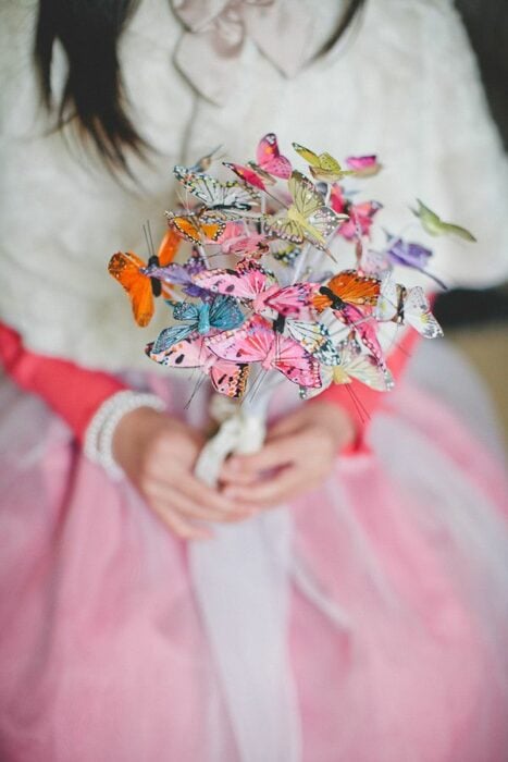 manos de una mujer en vestido blanco con rosa con un ramo hecho con mariposas en las manos 