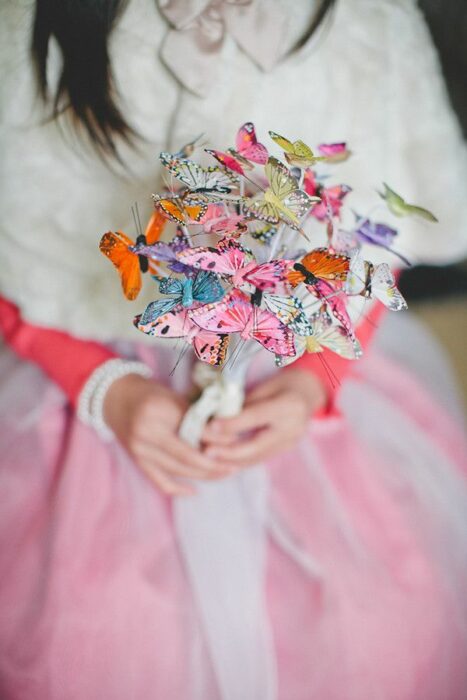 hands of a woman in white dress with rose with a bouquet made with butterflies in her hands 