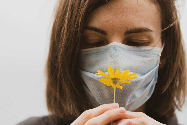 chica con cubre bocas oliendo una flor