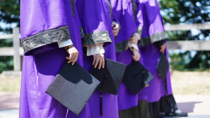 foto que muestra las manos de unas personas con birretes y togas en color morado