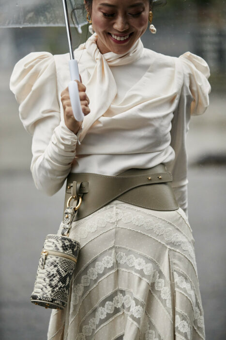 woman walking with an umbrella wearing a wide belt from which a bag hangs 