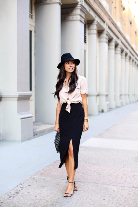 photo of a woman walking down a street wearing a skirt with a slit in the front and a fedora 