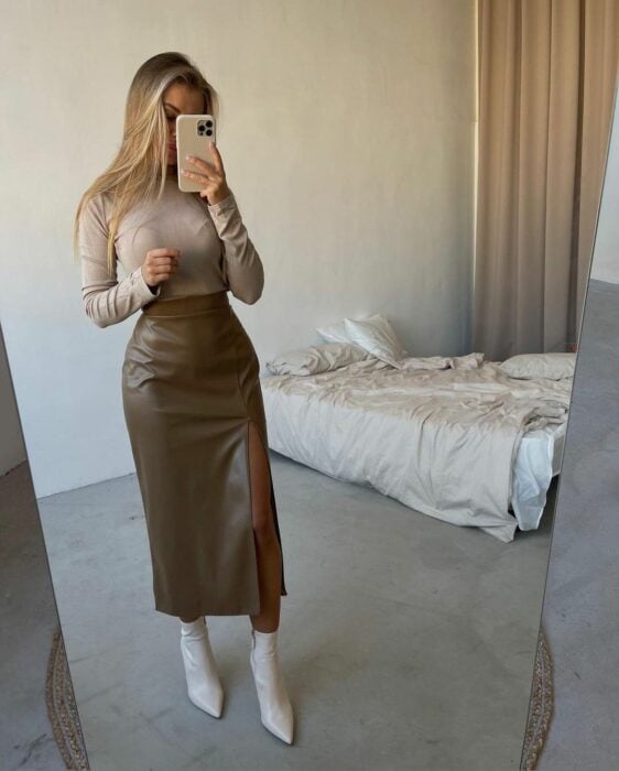 woman taking a photo in front of the mirror to show off her outfit with a vinyl skirt that matches a beige long-sleeved blouse 