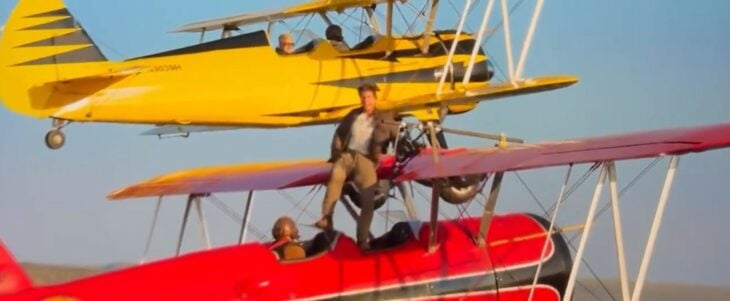 Tom Cruise parado en una avioneta que está en pleno vuelo 