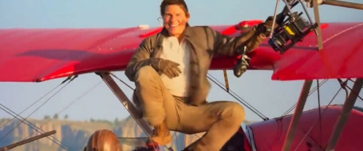 Tom Cruise on top of a red plane in full flight 