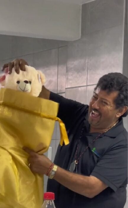 Foto de un hombre sacando un oso de peluche de una bolsa amarilla 