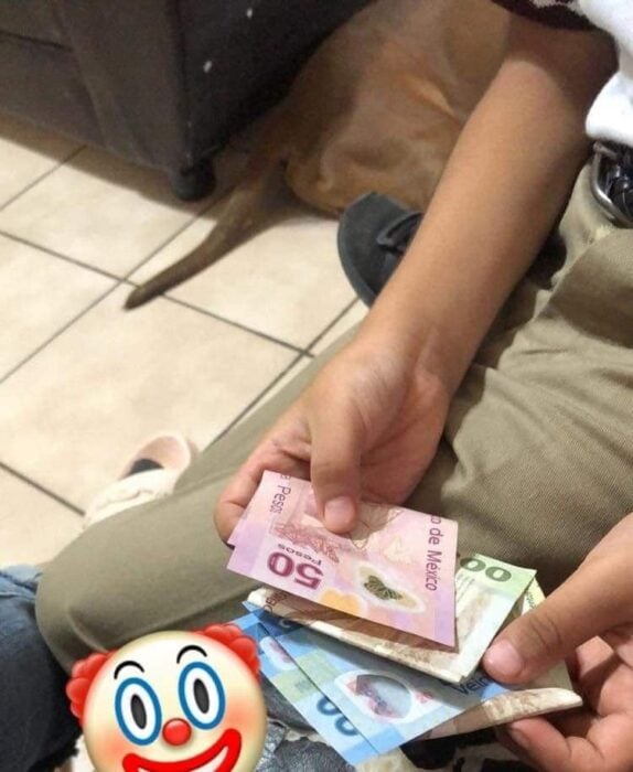 manos de un niño con billetes y un emoji de cara de payaso en su pierna 