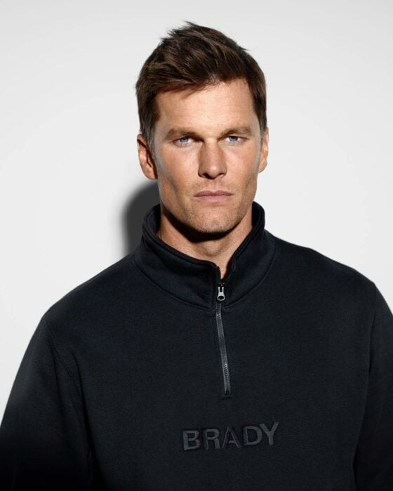 Tom Brady vestido con sudadera negra viendo a la cámara