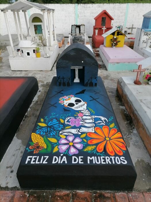 tumba con el dibujo de una catrina con flores y la frase "Feliz Día de Muertos" 