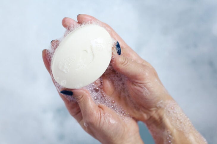 manos de una mujer con un jabón Dove rodeado de espuma 