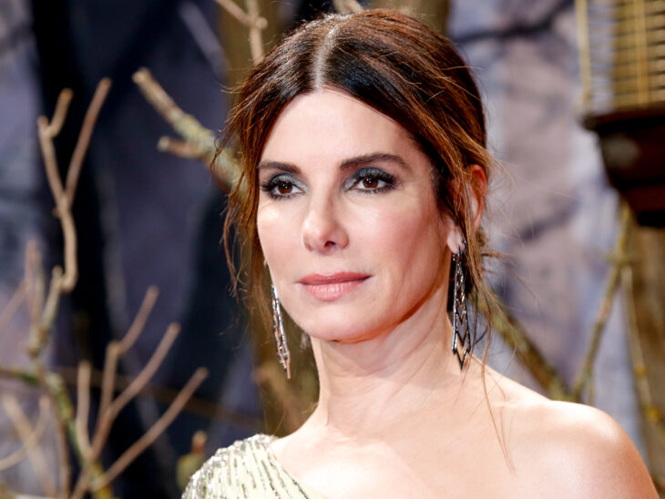 Sandra Bullock vestida con elegancia para una entrega de premios lleva el cabello recogido en un chongo luciendo aretes largos y un vestidos en tono beige maquillaje discreto