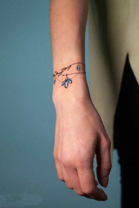imagen de la mano de una chica que muestra un tatuaje de pulsera con diamantes de color azul cielo 