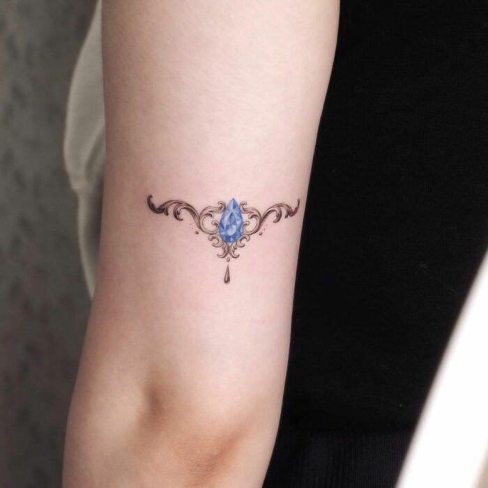 Fotografía del brazo de una mujer mostrando un tatuaje de un pequeño brazalete de diamantes en color azul 