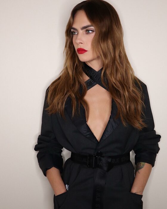 Cara Delevingne in a black dress leaning against the wall