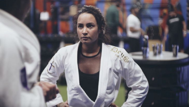 Demi Lovato vestida con uniforme de artes marciales lleva un traje blanco y debajo una blusa negra 