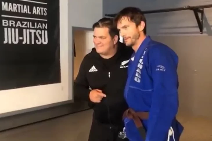 Ashton Kutcher vestido con un uniforme de artes marciales azul junto a su entrenador