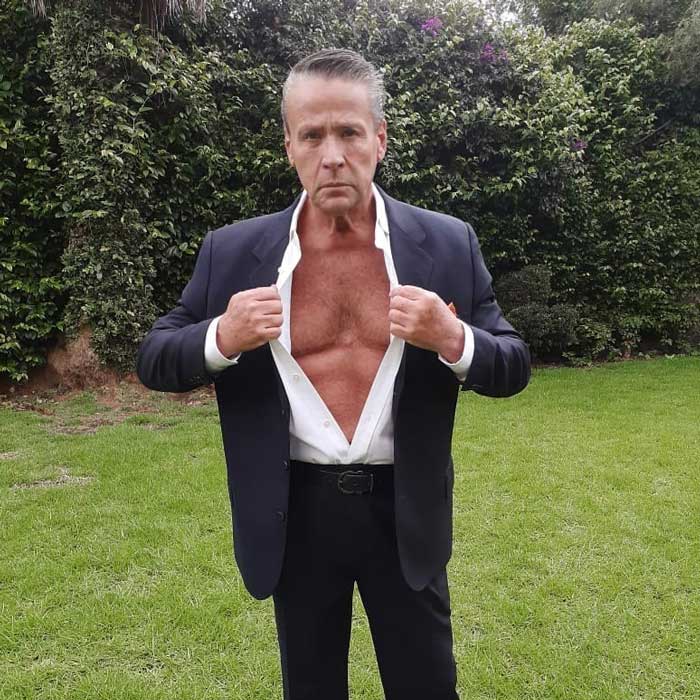 Photo of Alfredo Adame opening his shirt standing in a house garden 