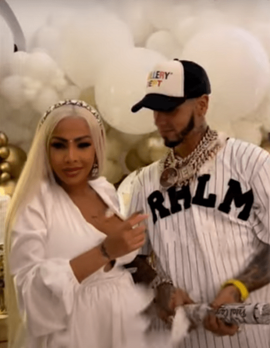 Anuel A. A. y su esposa Yailin La más viral en la fiesta de revelación de sexo de su hija ambos vestidos de blanco rodeados de globos dorados y blancos 