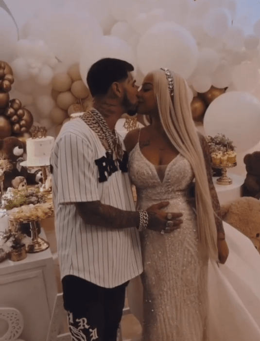 Anuel A. A. y su esposa Yailin La más viral en la fiesta de revelación de sexo de su hija ella porta un vestido largo de noche de color blanco lleva el cabello rubio platinado suelto y largo el trae una camiseta tipo jugador de beisbol blanca con rayas negras