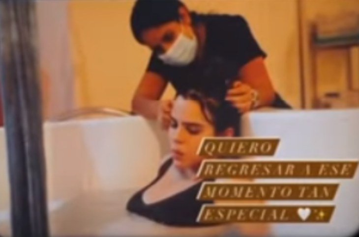Yuya en trabajo de parto es assitida por una enfermera mientras ella está sumergida en una tina blanca con agua lleva un topo negro y el cabello recogido