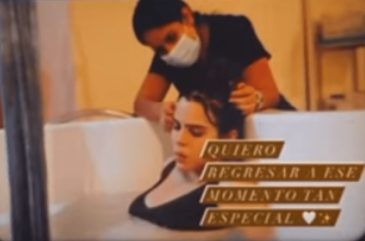 Yuya in labor is assisted by a nurse while she is submerged in a white tub of water, she wears a black mole and her hair is tied up