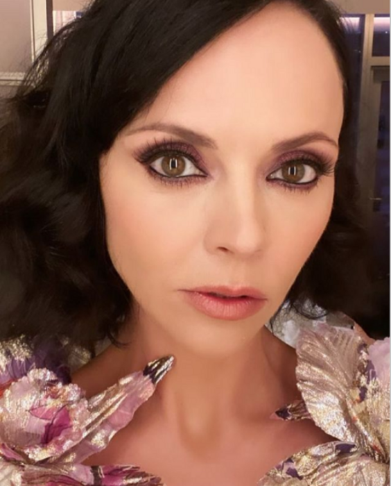 Christina Ricci in front of the camera showing off her face in the foreground, wears discreet makeup and a flowered blouse that highlights her light eyes