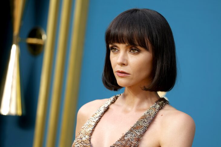 The actress Christina Ricci posing for the cameras on a red carpet has very short straight hair and wears a sleeveless gold dress her makeup is discreet