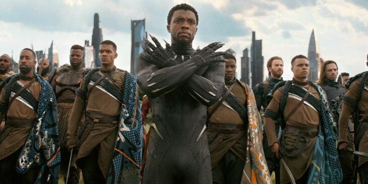 Imagen de la primer cinta de Black Panther del actor Chadwin Boseman vestido de pantera negra con habitantes de wakanda detrás
