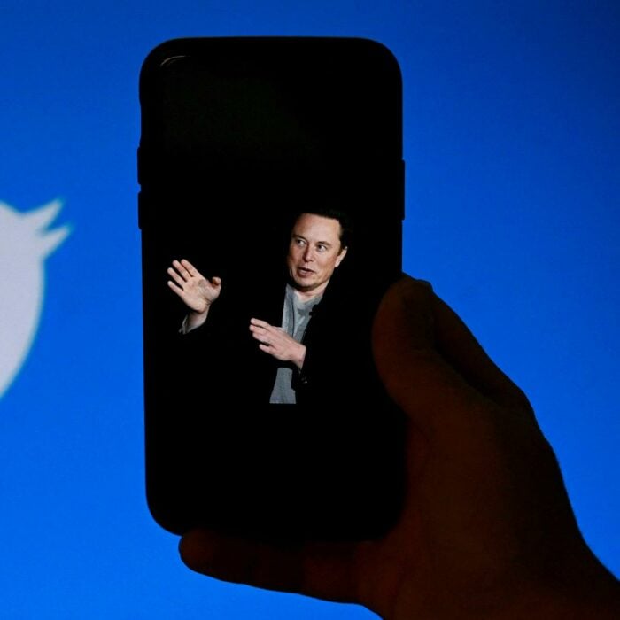 MAno con un celular que muestra la imagen de Elon Musk con el logo de Twitter de fondo 