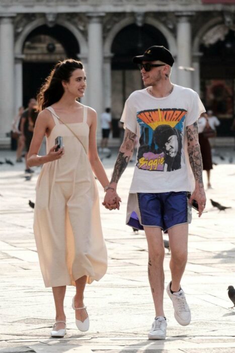 Margaret Qualley caminando de la mano de Pete Davidson por una calle que parece ser la plaza de algún lugar 