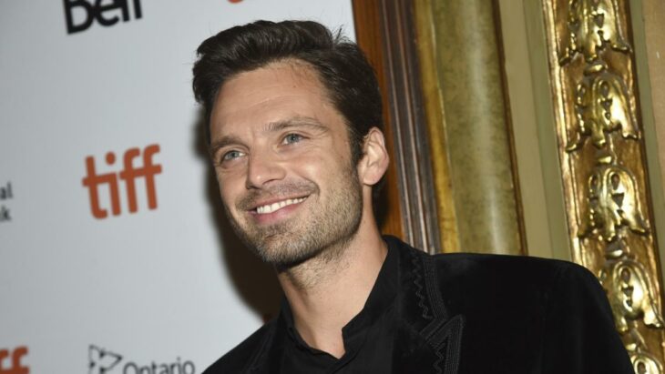 Sebastian Stan esta en una alfombra roja lleva un saco negro con una camisa oscura esta sonriendo