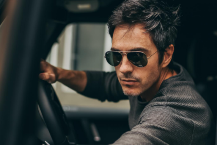 Mauricio Ochmann fotografiado conduciendo una camioneta lleva lentes oscuros y una sudadera gris el cabello corto y alborotado