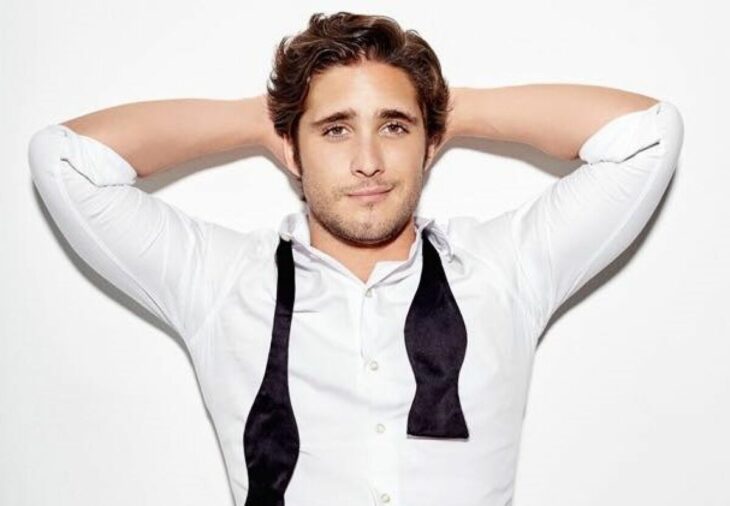 Diego Boneta posa para la cámara acostado de frente lleva una camisa blanca con un moño deshecho negro tiene sus manos debajo de su cabeza